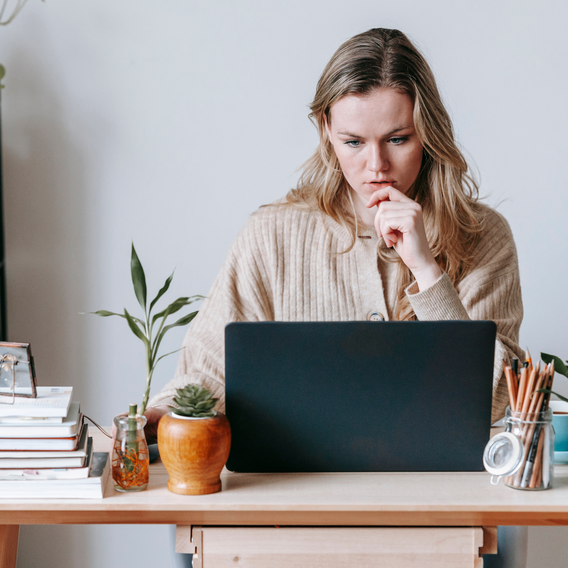 Eine Frau sitzt an einem Schreibtisch und arbeitet konzentriert an einem Laptop. Sie scheint tief in Gedanken versunken, was auf intensiven Fokus und Konzentration hinweist. De