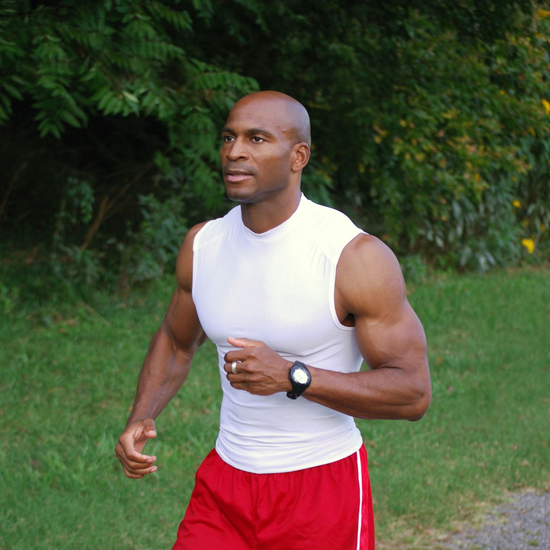 Ein athletischer Mann, der im Freien joggt, bekleidet mit einem weißen ärmellosen Shirt und roten Shorts, mit einem Fokus auf Fitness und workout.